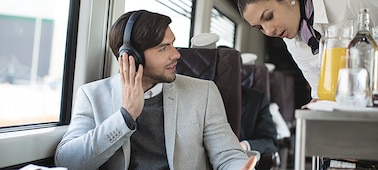    A male on the train placing his right hand over right earcup, while speaking to a female train attendant